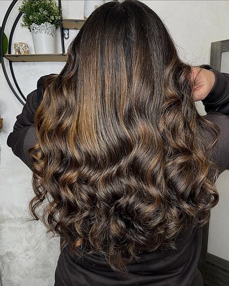 Capelli lunghi mossi con balayage caramello su base castano scuro